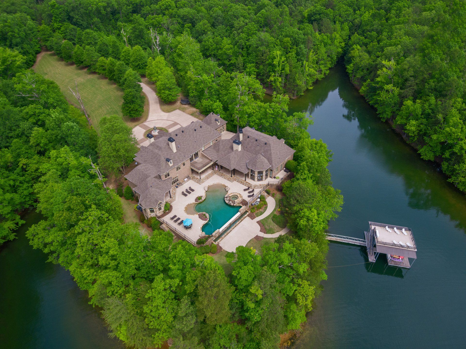 An aerial view of a large house on a small island in the middle of a lake surrounded by trees.