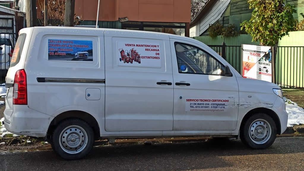 Furgoneta de carga blanca estacionada en una calle con anuncios comerciales a los lados.