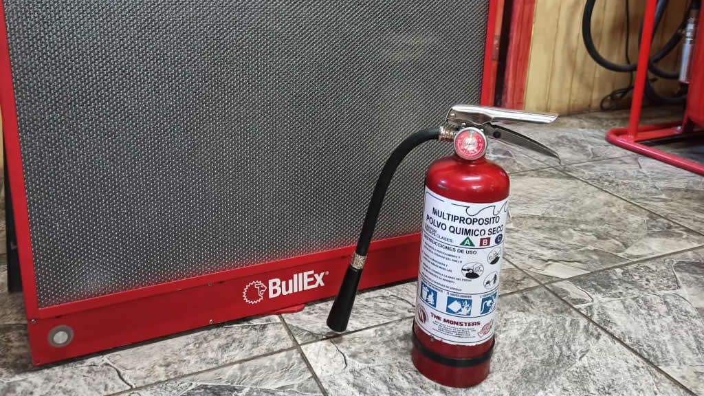Extintor rojo junto a un altavoz rojo, sobre un suelo de baldosas.