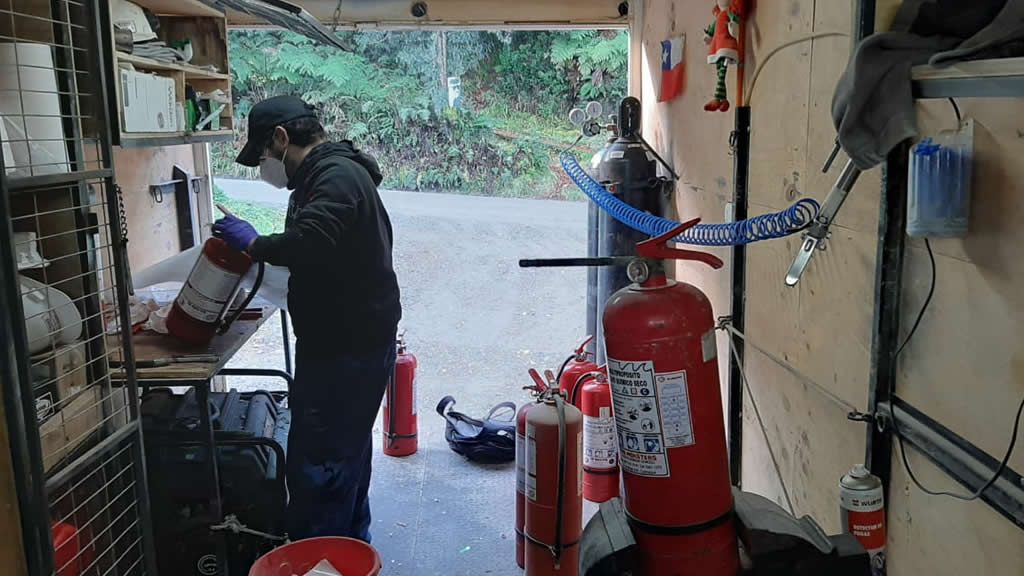 Persona con máscara y guantes trabajando dentro de un vehículo, posiblemente reparando extintores de incendios.