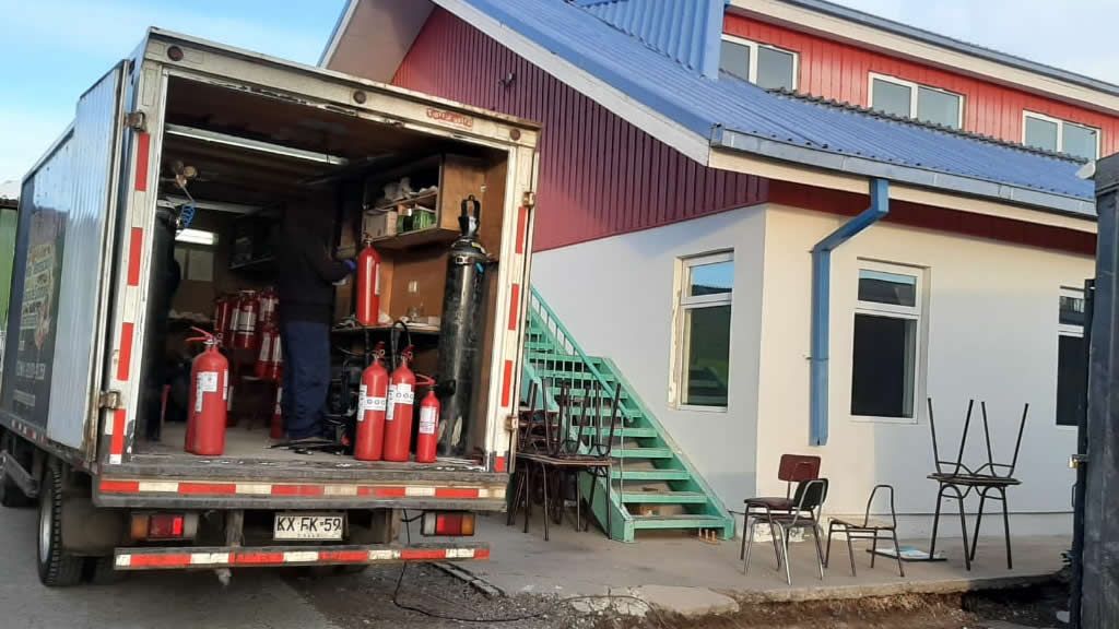 Camión descargando extintores cerca de un edificio con paredes rojas y blancas y una escalera verde.