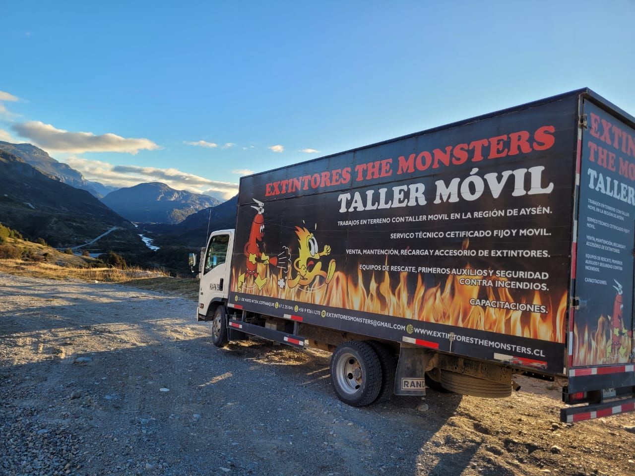 Camión taller móvil con gráficos monstruosos, estacionado en un pintoresco paisaje montañoso.