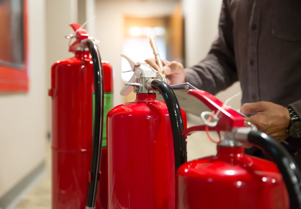 Persona inspeccionando extintores rojos en el pasillo de un edificio.