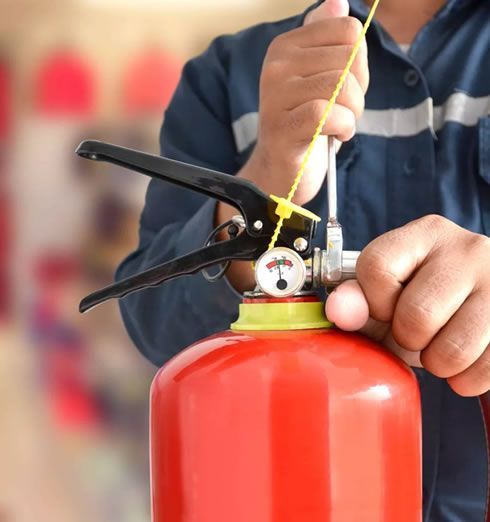 Persona quitando el pasador de seguridad de un extintor rojo; vista de cerca.