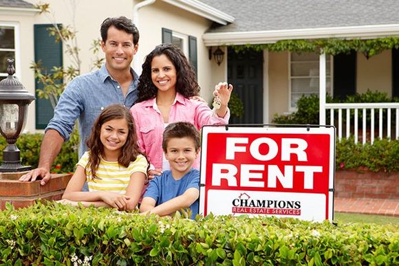 A family of four poses by a For Rent sign in their front yard.