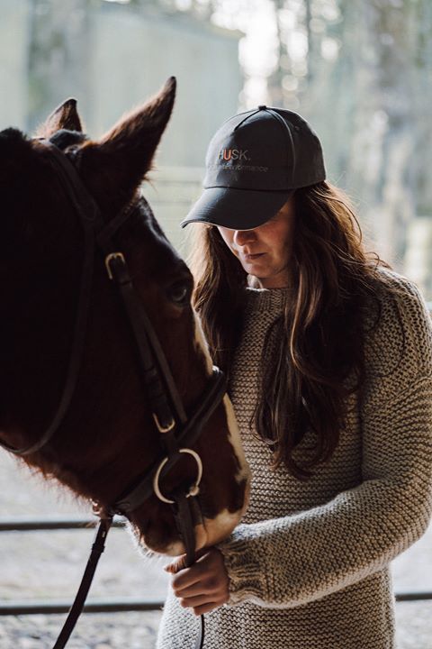 a woman in a baseball cap is petting a brown horse .