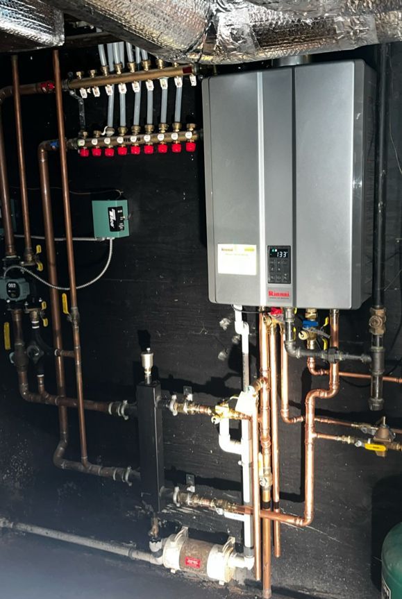 Plumbing system with a gray tankless water heater, copper pipes, valves, and a red and gold manifold.