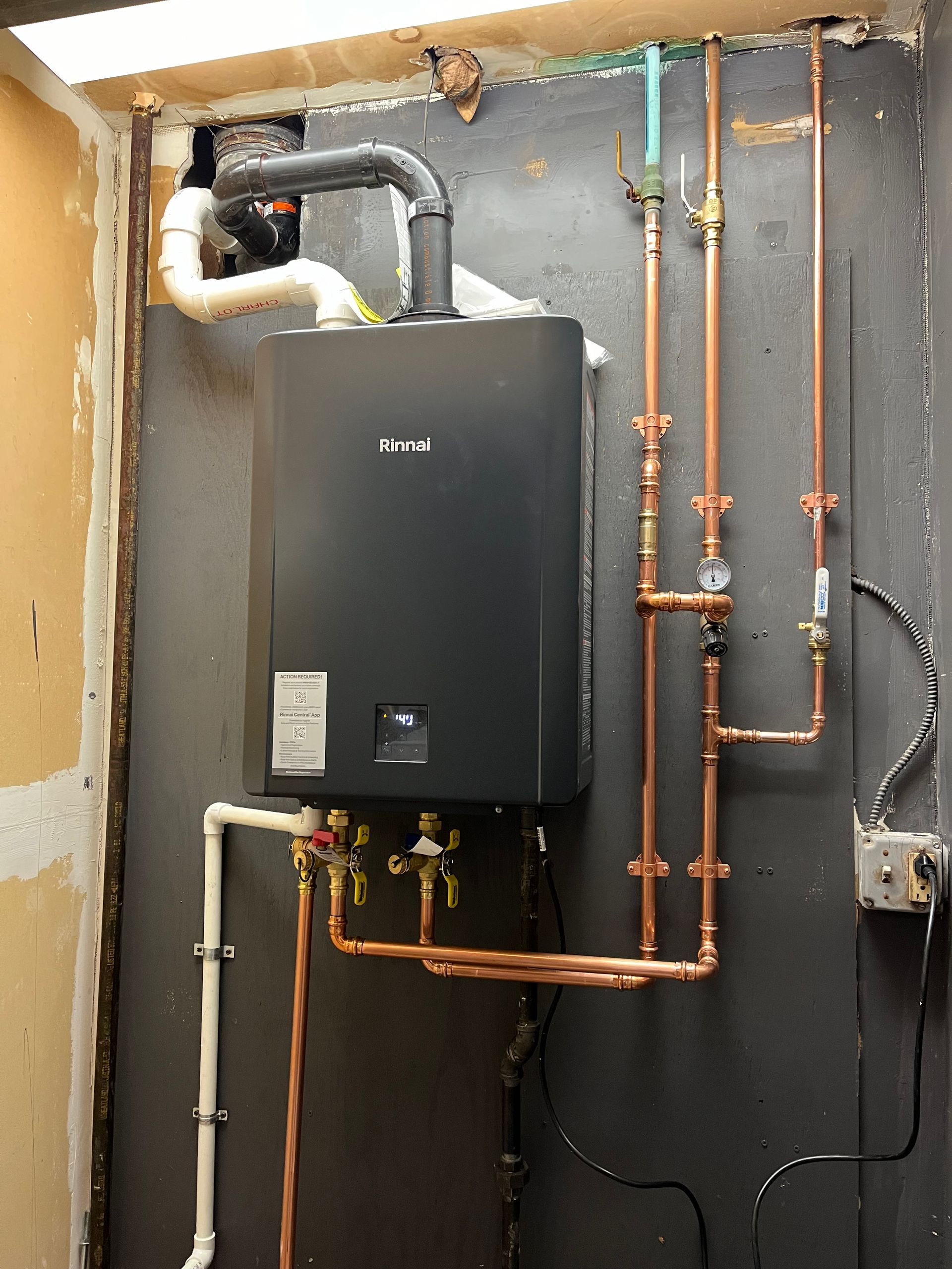 A wall-mounted, black tankless water heater with copper piping.