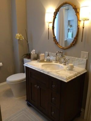 Elegant bathroom with dark brown vanity, marble countertop, gold mirror, and sconces.