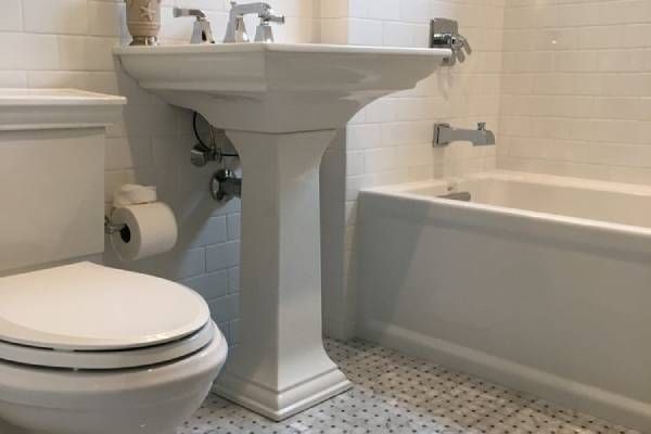 White bathroom with a pedestal sink, toilet, and bathtub.