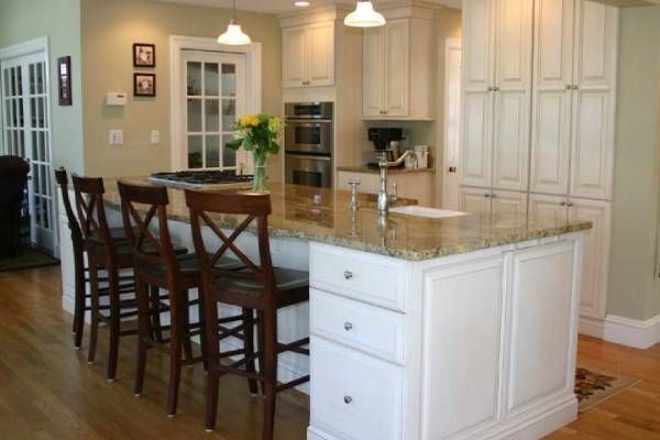 Kitchen with white cabinets, wood island with bar stools, granite countertop, and hardwood floors.