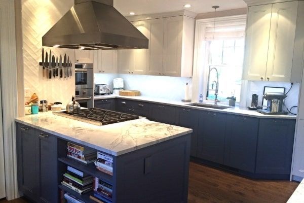 Modern kitchen with dark blue and gray cabinets, island with stovetop, and stainless steel range hood.