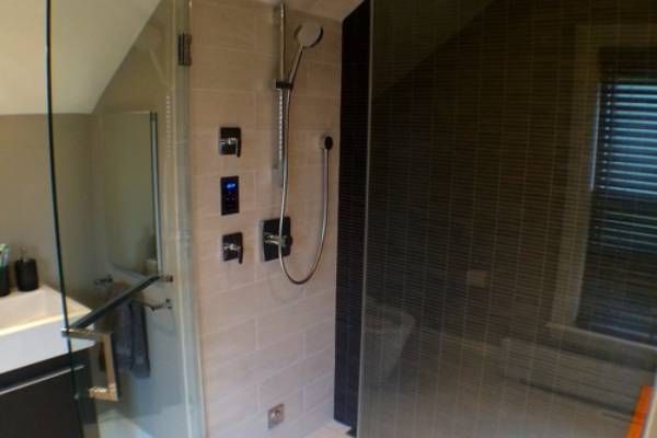 Modern shower with glass doors, tiled walls, and shower fixtures; window with blinds visible.