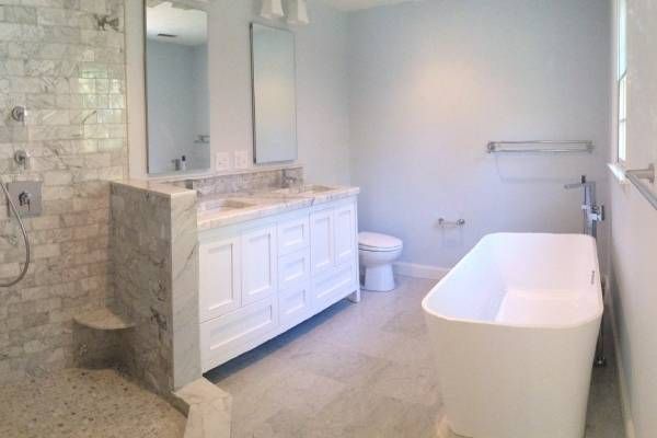 Bathroom with white vanity, soaking tub, toilet, shower with marble tile, and light blue walls.