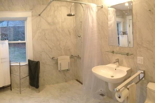 Accessible marble bathroom with shower, sink, toilet, and window. Includes grab bars and low fixtures.