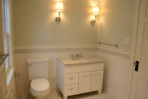 Small bathroom with white vanity, toilet, and sconce lighting on a light green wall with white trim.