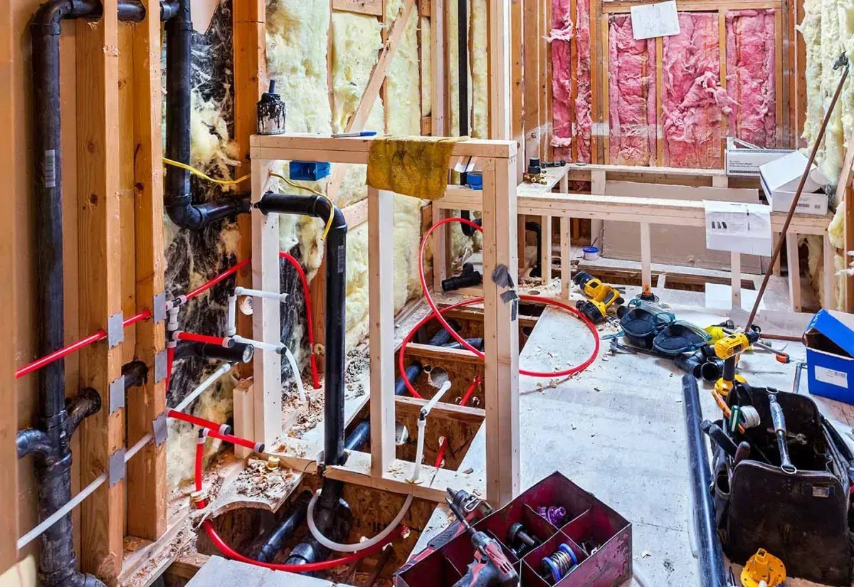 Bathroom under construction with exposed plumbing, wooden frame, insulation, and tools scattered about.