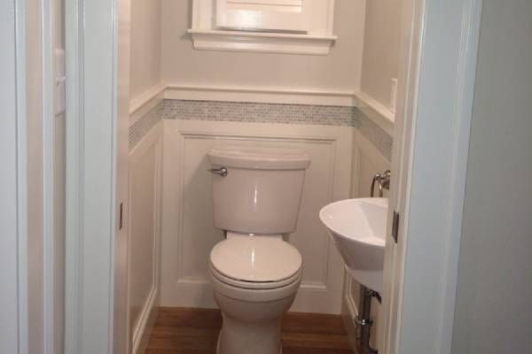 Small bathroom with toilet and sink, white walls with wainscoting, and wooden floor.