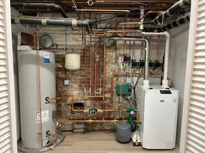 Plumbing and heating system with water heater, boiler, and copper pipes in a utility room.