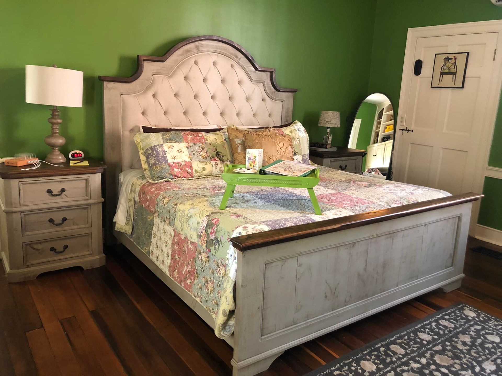 A bedroom with a bed , nightstand , lamp and a green tray on the bed.
