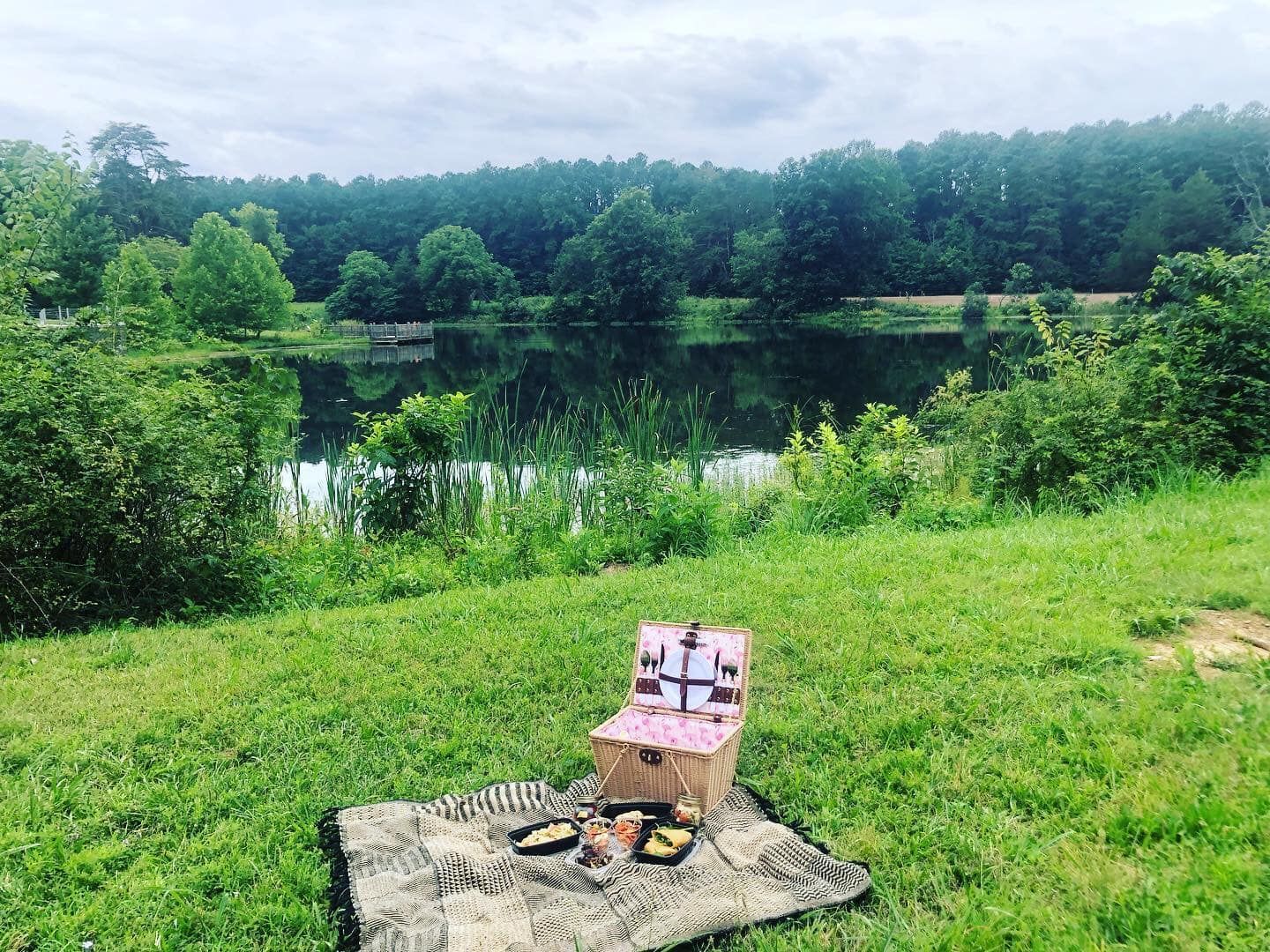 A picnic basket is sitting on a blanket in front of a lake.