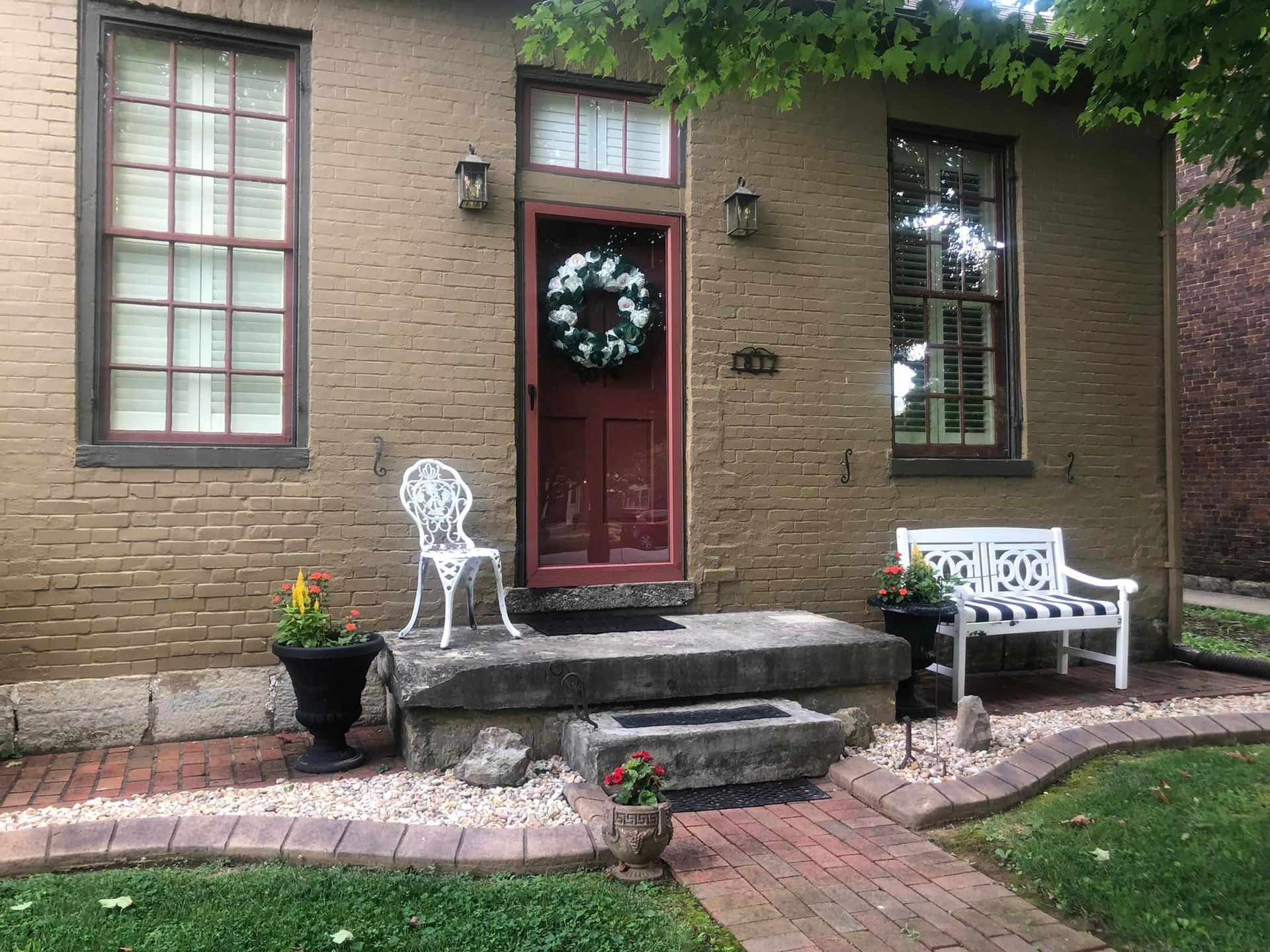 A brick house with a red door and a white bench in front of it.