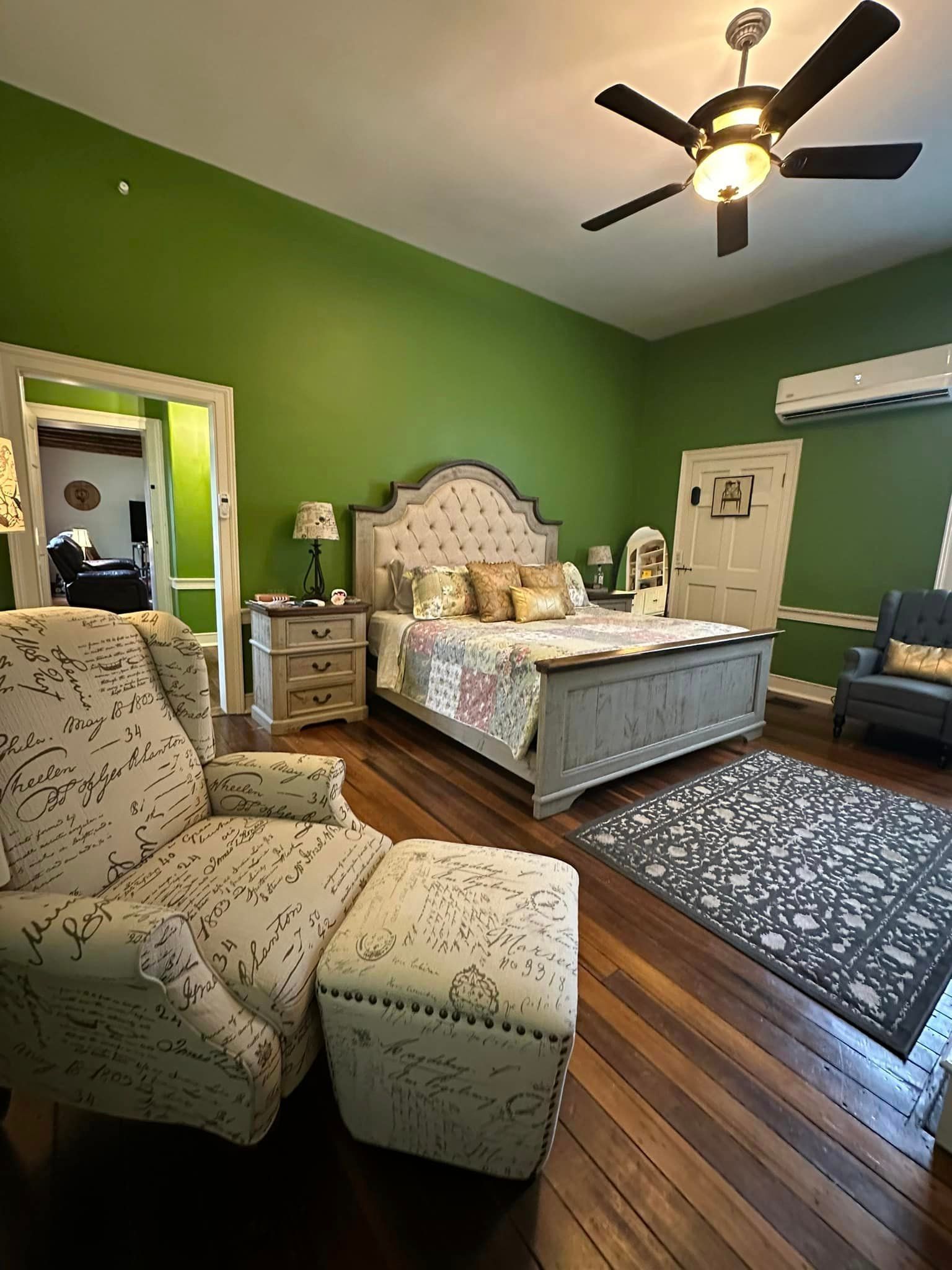 A bedroom with green walls , a bed , a chair , and a ceiling fan.