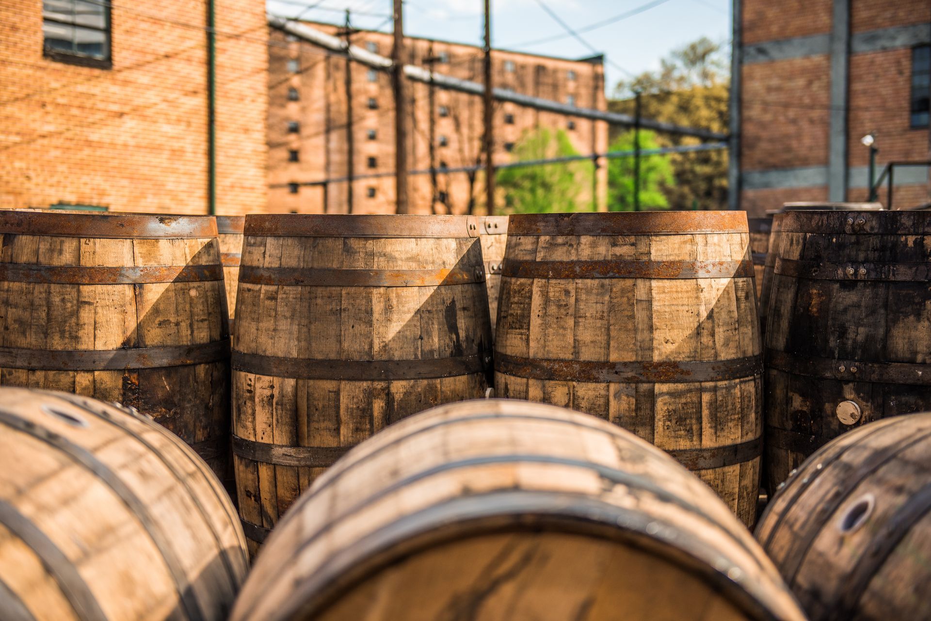 A bunch of wooden barrels are stacked on top of each other in front of a brick building.