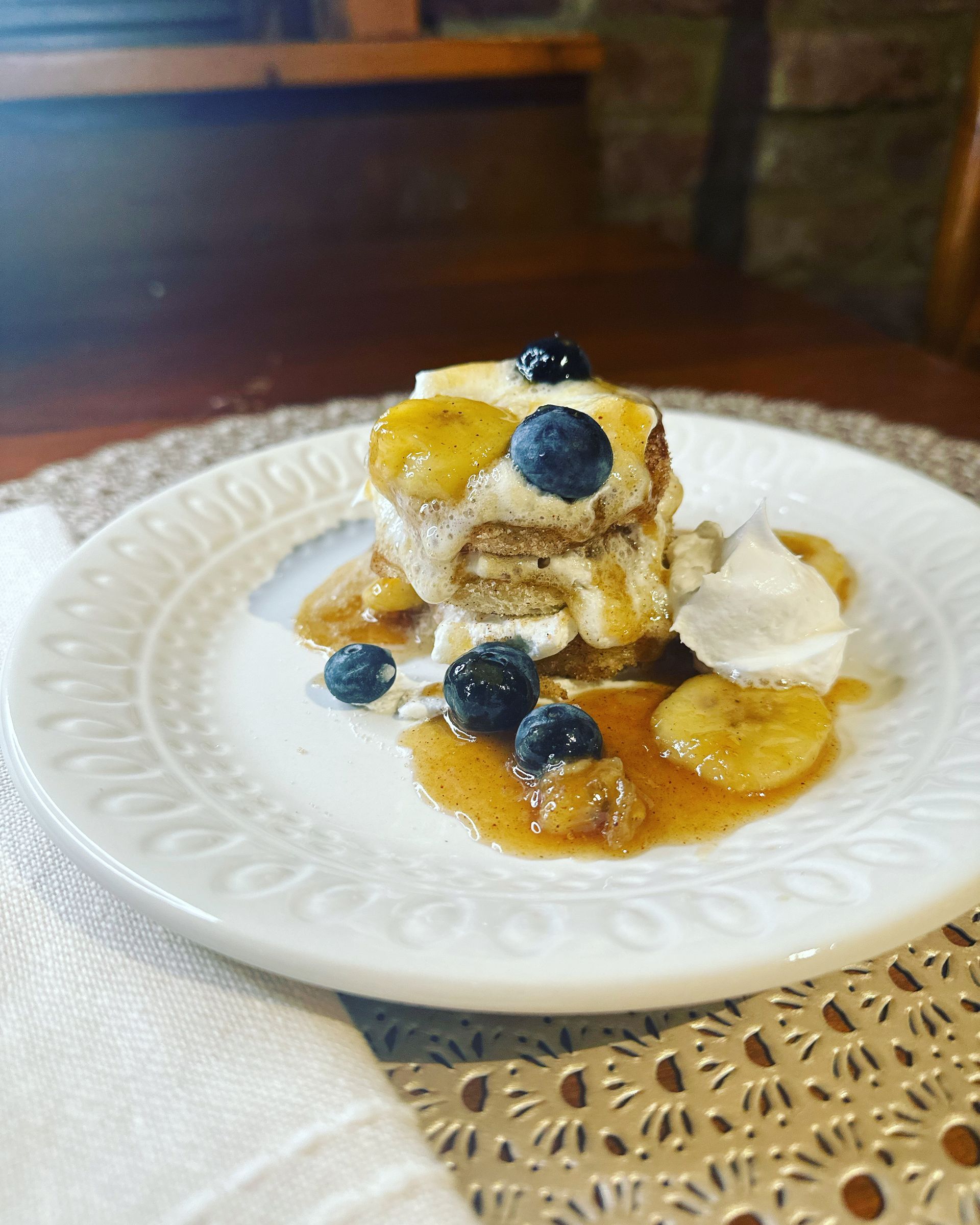 A white plate topped with a stack of pancakes with blueberries and bananas.