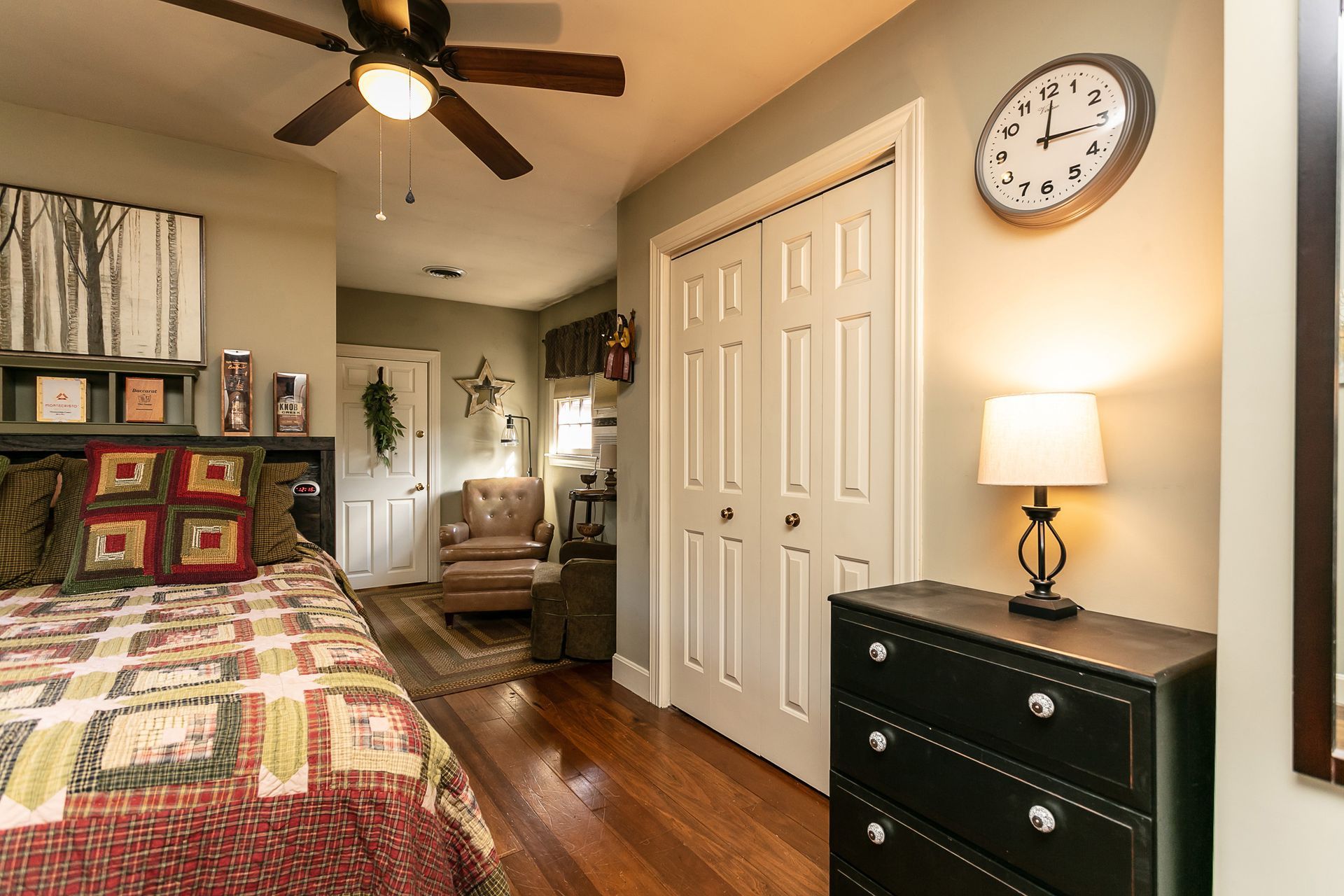 A bedroom with a bed , dresser , lamp and a clock on the wall.