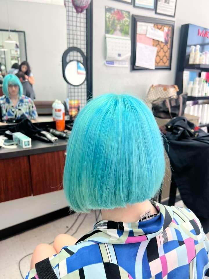 Back view of person with turquoise bob haircut in a salon, looking in a mirror.