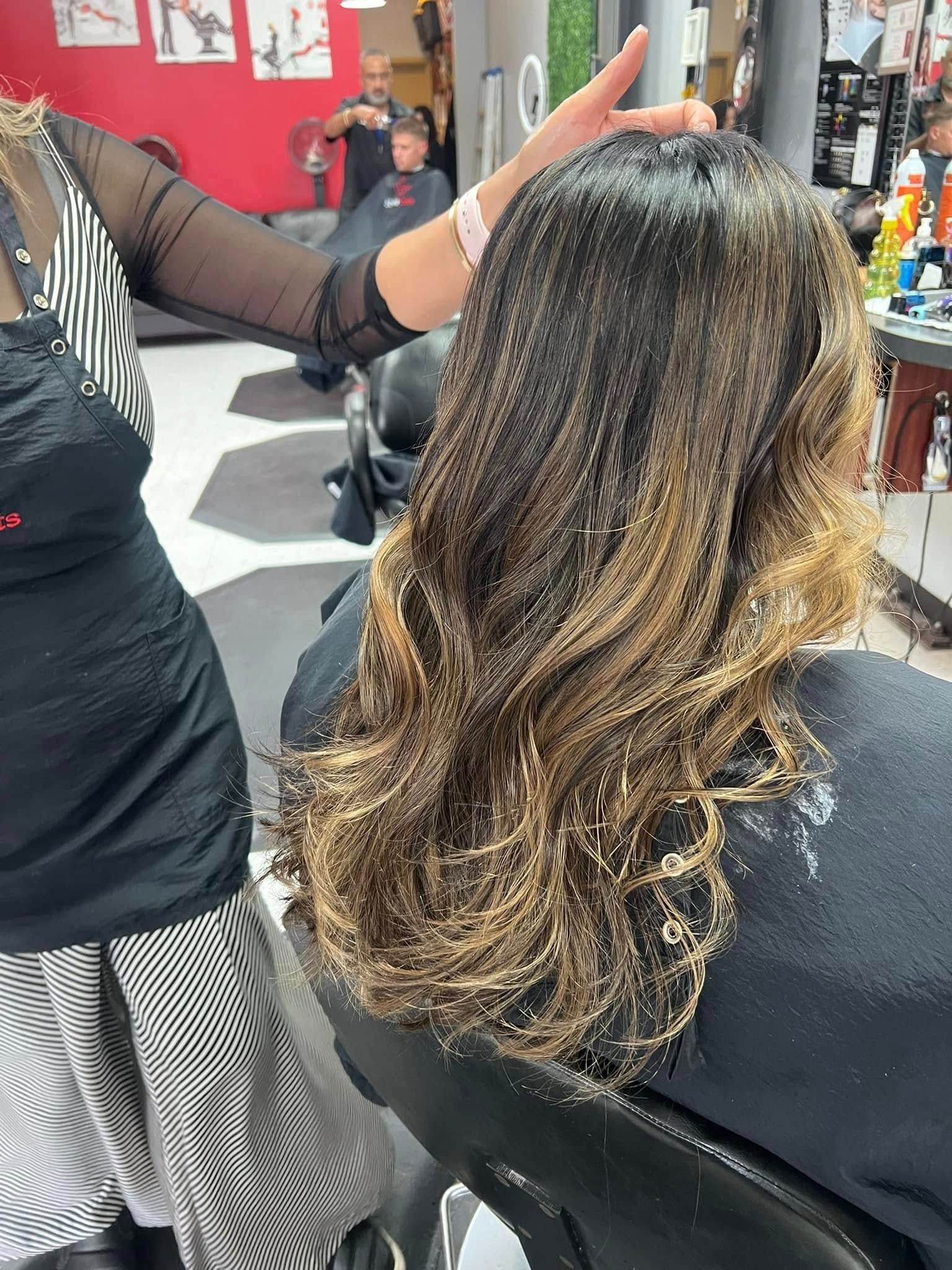 Woman in a salon chair with hair being styled by a stylist. Hair has blonde highlights.