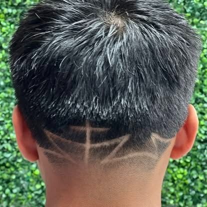 Boy's dark hair with geometric hair design shaved into the back, against a green background.