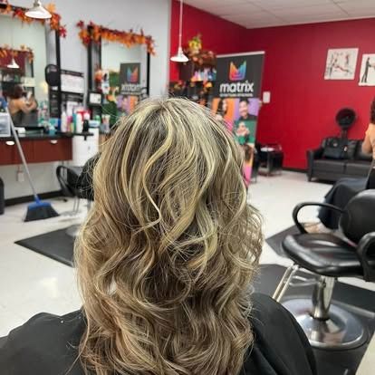 Blonde hair with highlights styled in waves. Salon setting with Matrix banner and red wall.
