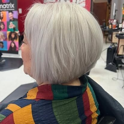 Woman with short, light-gray bob haircut sits in a salon chair. She wears a colorful striped shirt.