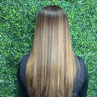 Woman with long, straight brown hair with highlights against a green textured wall.