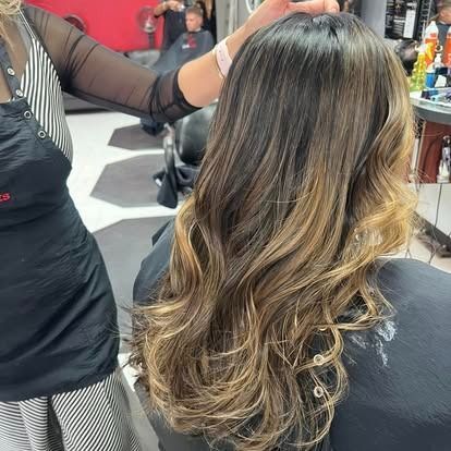 Hair stylist working on long brown hair with blonde highlights at a salon.