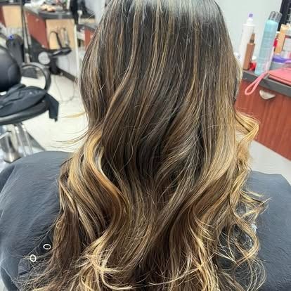 Woman's long, wavy hair with brown and blonde highlights, styled in a salon.