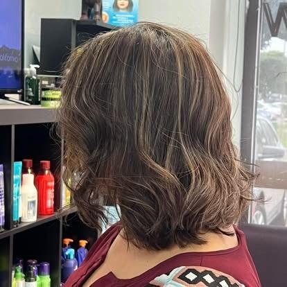 Woman with wavy brown hair and blonde highlights, in a hair salon.