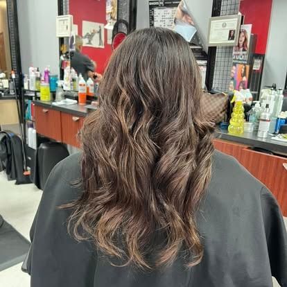 Person with wavy brown hair at a salon, wearing a black cape.