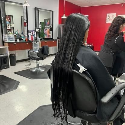 Woman in a salon chair with long, wet hair, facing away from the camera. The setting is a hair salon.