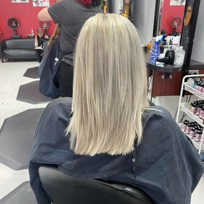 A person with long, blonde hair sits in a salon chair, ready for a haircut.