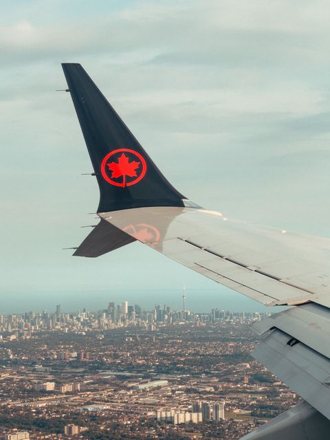 Airplane wing with Air Canada logo flying over a city skyline under a cloudy sky
