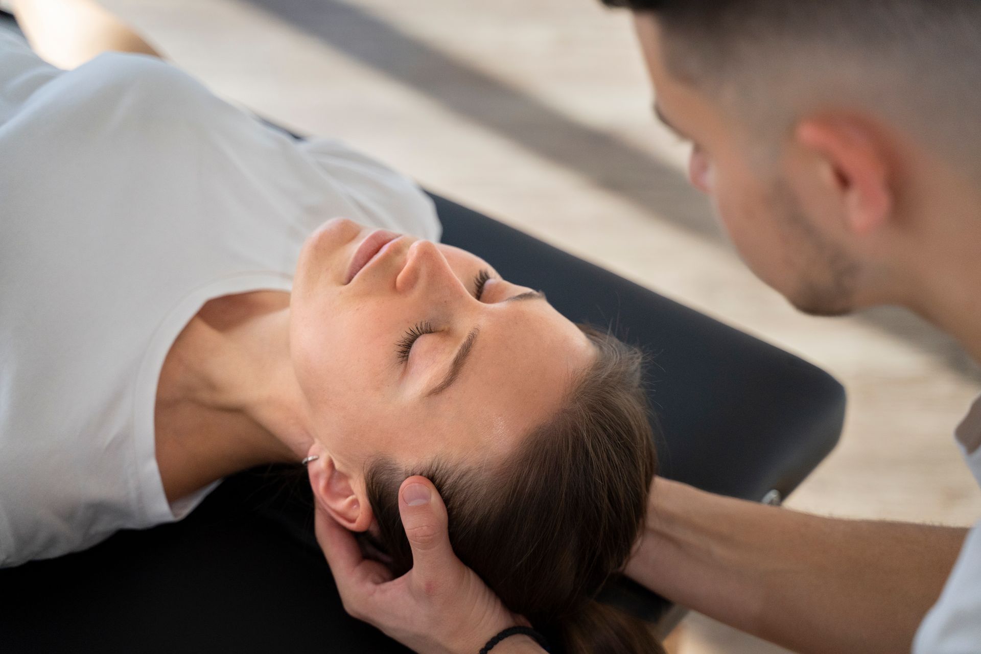 A woman is laying on a table getting a head massage from a man.
