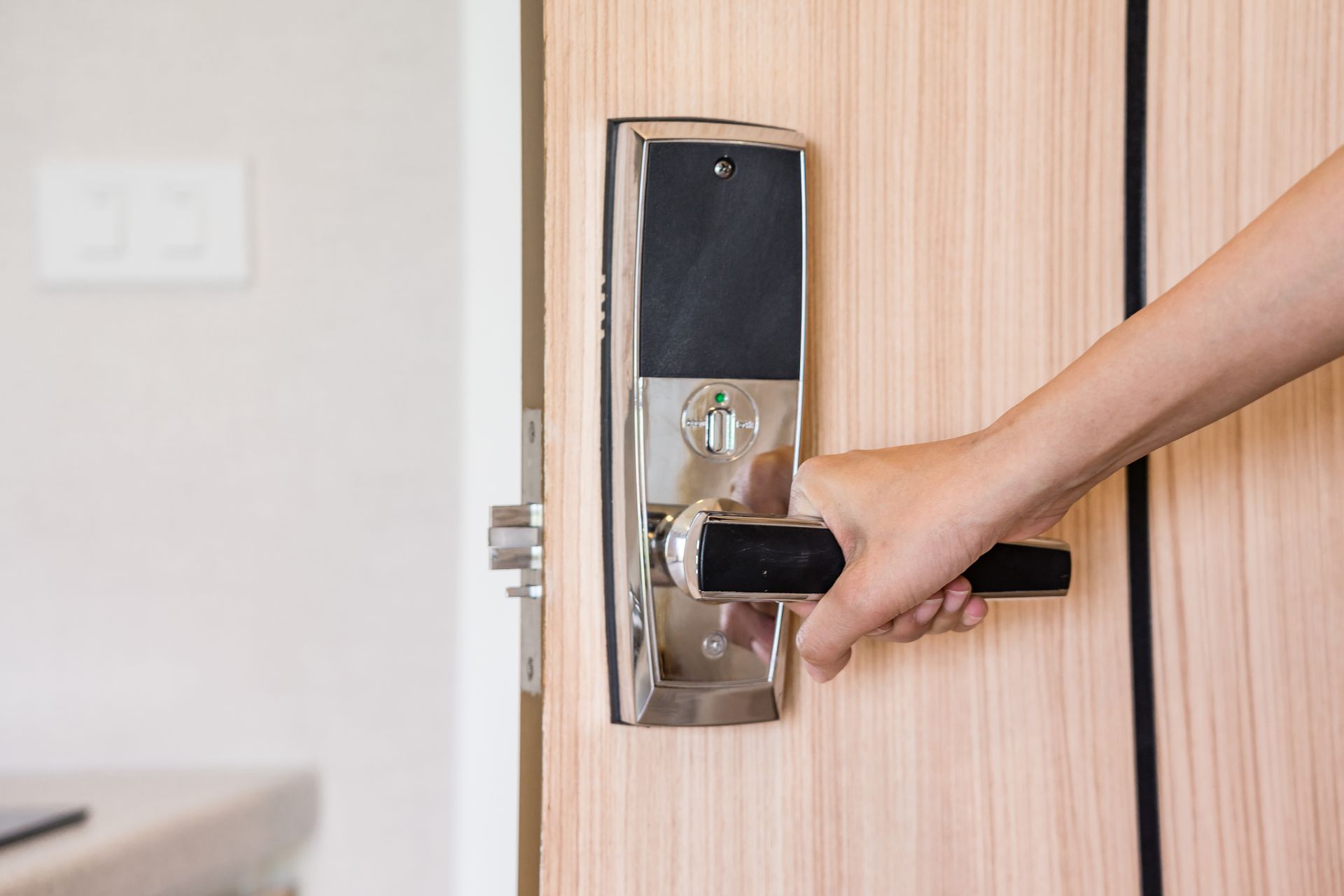 Hand turning a black door lever on a light wood door, opening a room.