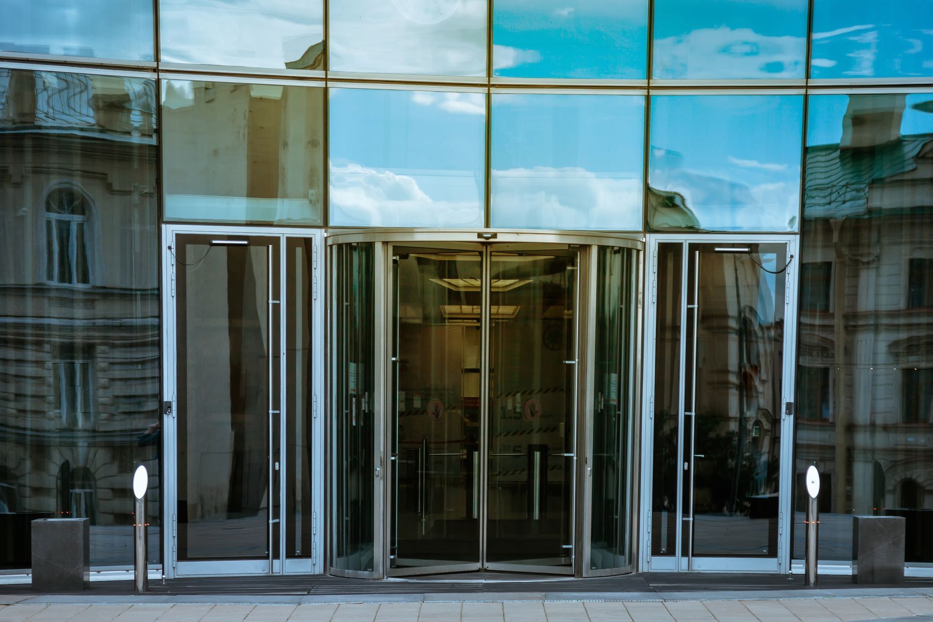 Glass-front building entrance with revolving doors and reflections of the street and sky