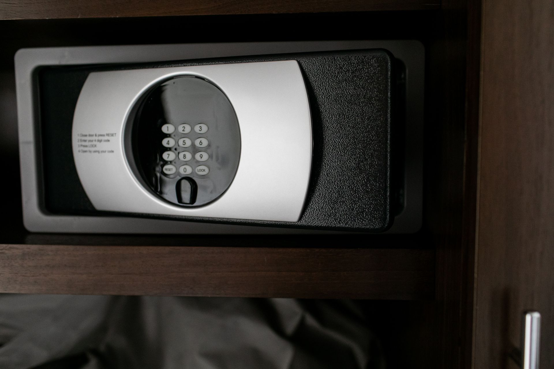 Silver and black hotel safe with keypad, built into a dark wooden cabinet.