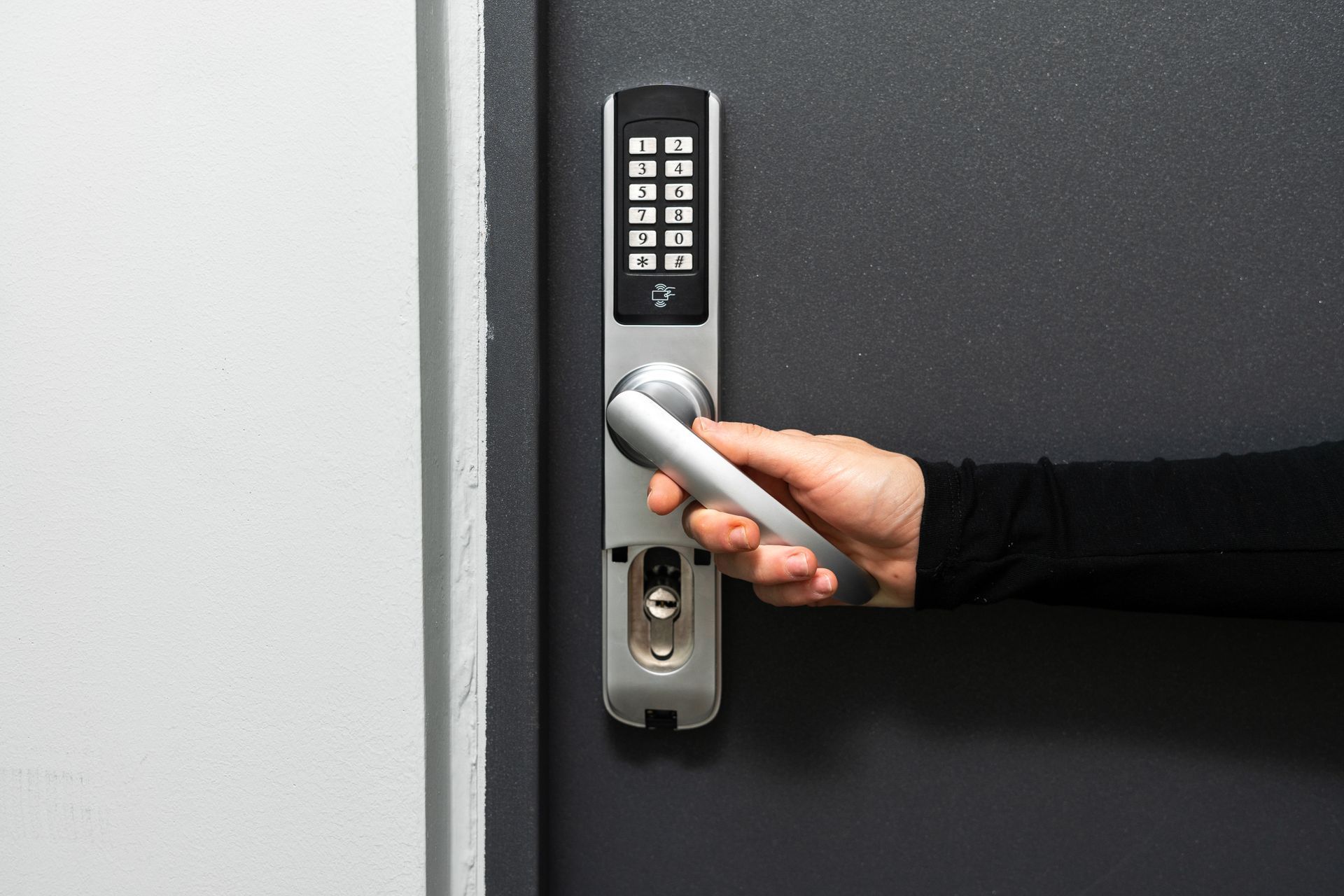 Person's hand on a silver handle of a black door with a keypad lock.