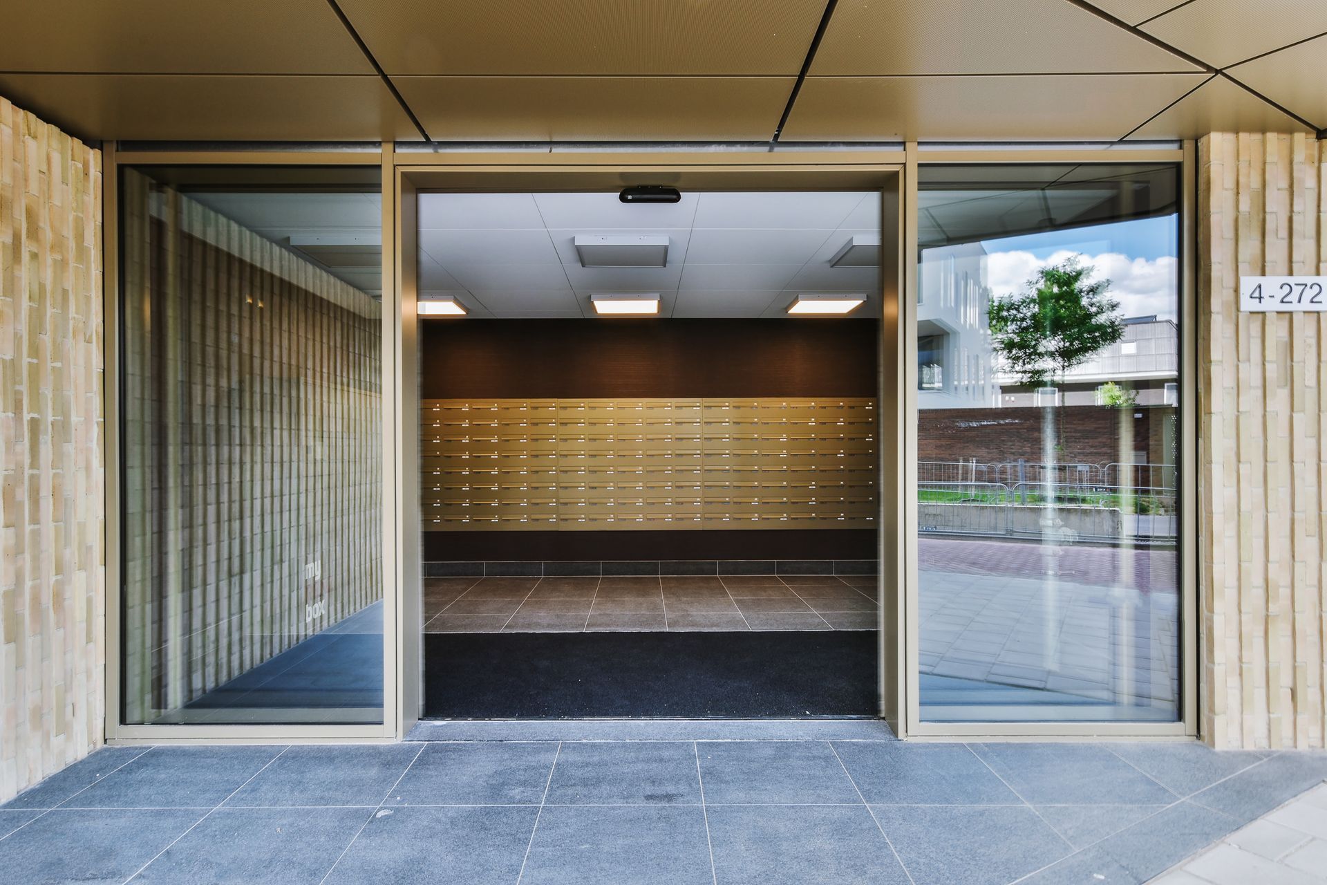Automatic doors open to an entrance with mailboxes inside a modern building.