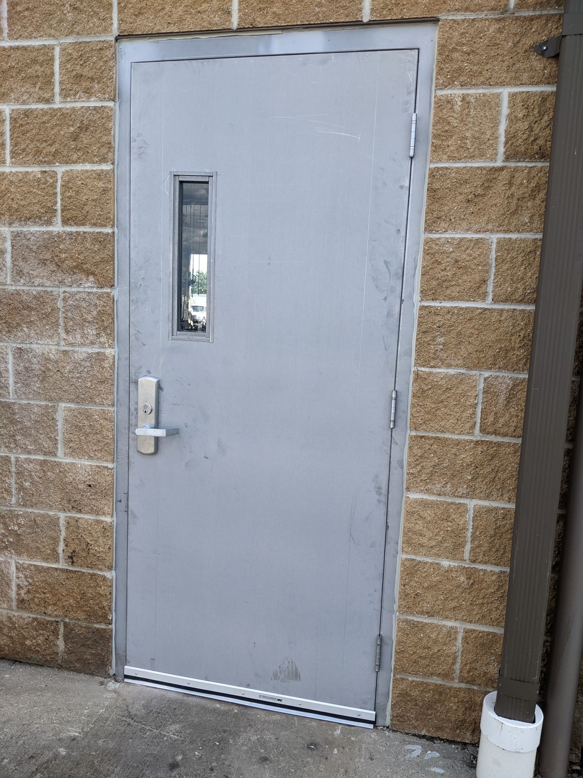 A gray door with a small window is on a brick wall.
